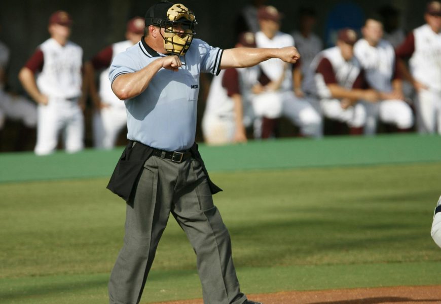 Umpire in action on baseball field with team players in the background.