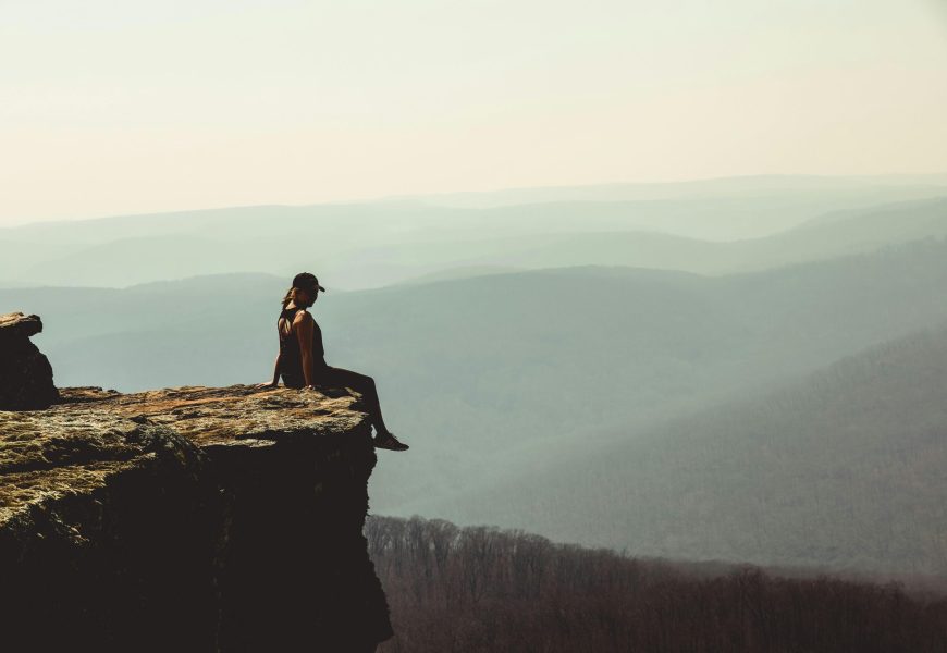 Woman sitting on a cliff edge overlooking a vast mountain landscape in Arkansas.