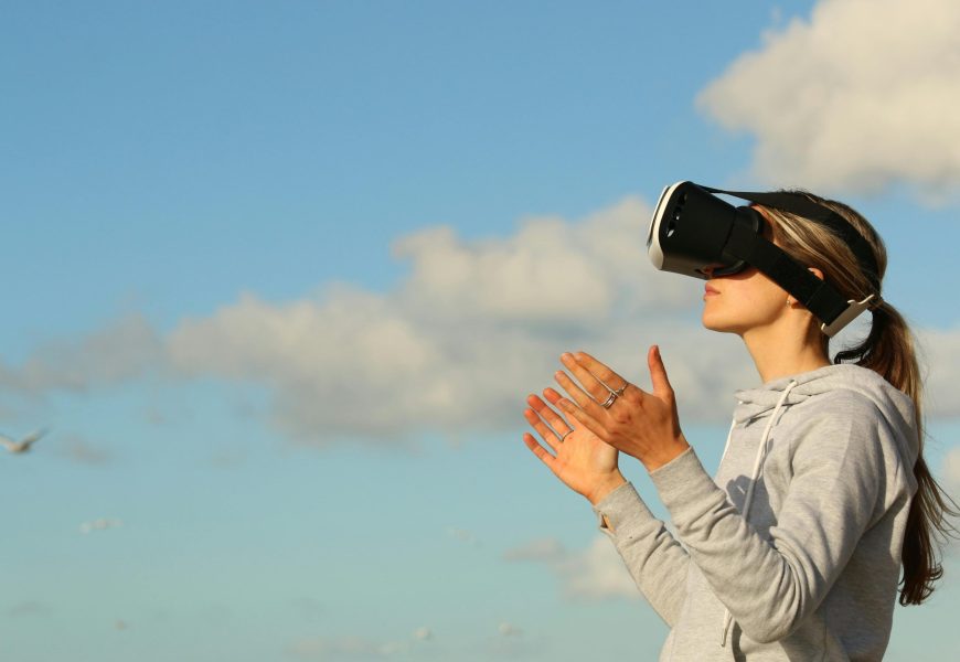 Woman using VR headset outdoors, exploring virtual reality under a clear blue sky.