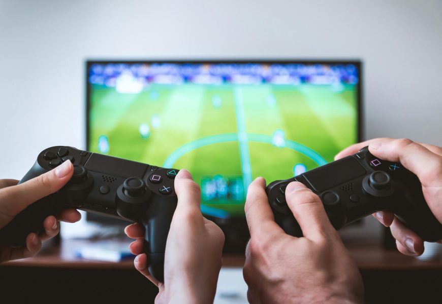 Close-up of hands holding gaming controllers in front of a TV. Engaged in a video gaming session.