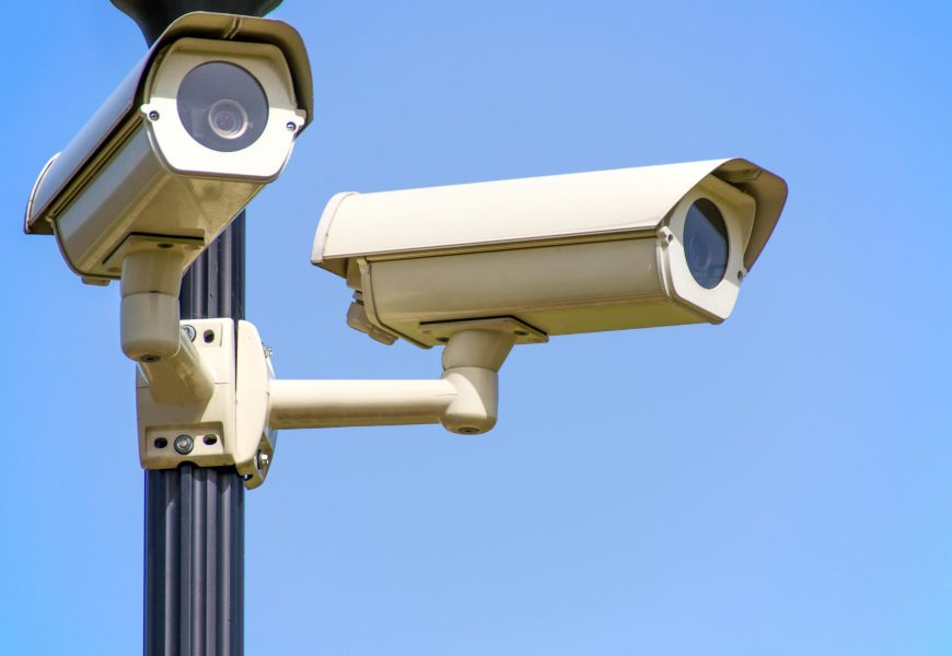Outdoor security cameras mounted on a pole against a clear blue sky, ensuring vigilant surveillance.